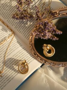 earrings and necklace on top of book, flower, and mirror 